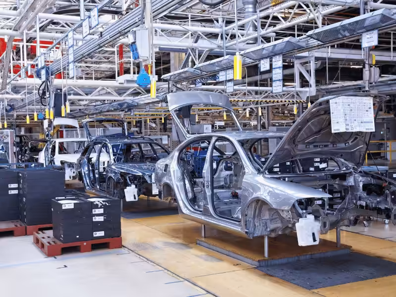 Multiple car chassis, including sedans and station wagons, are lined up on a yellow track on a car assembly line.