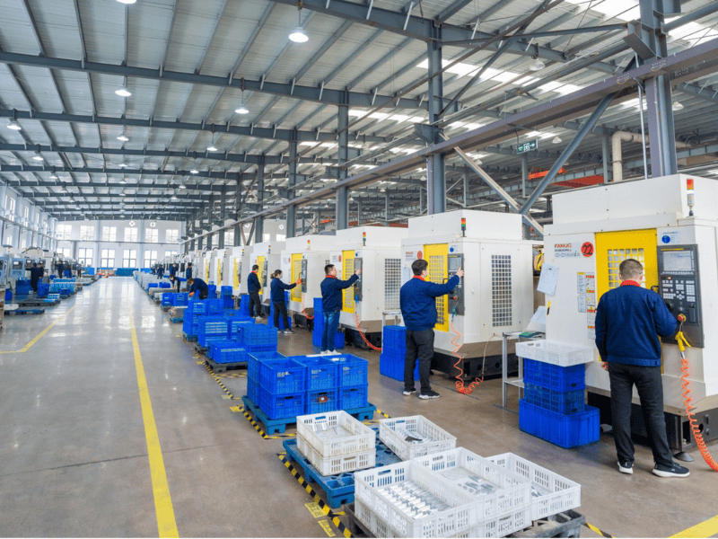 A modern industrial factory floor with a long row of FANUC CNC machines and workers in blue uniforms.
