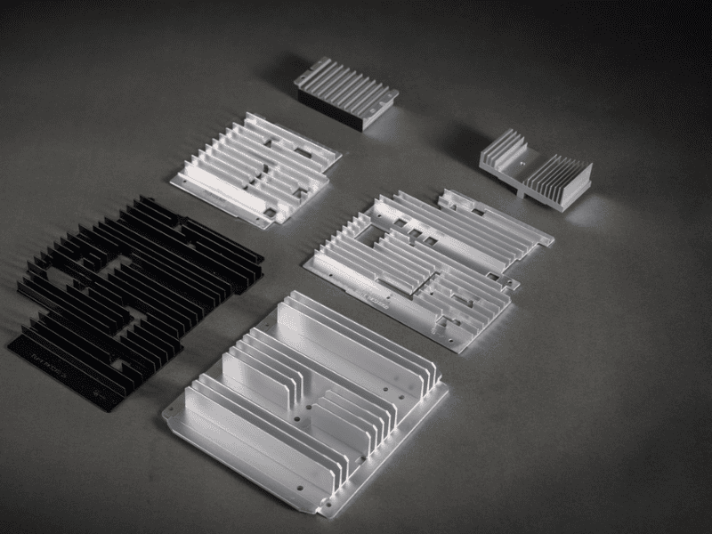 A variety of silver and black aluminum extruded heat sinks arranged on a dark grey surface.