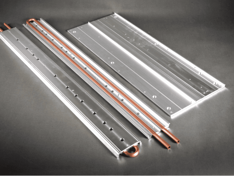 An assortment of silver and black aluminum extruded heat sinks in various sizes and fin configurations, arranged on a dark grey surface.